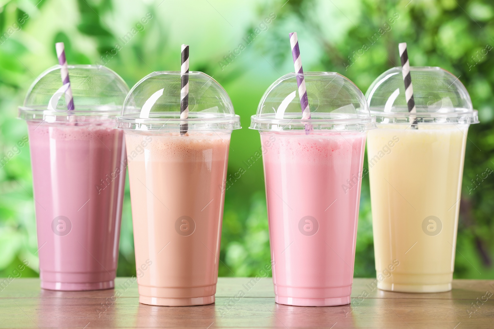 Tasty milkshakes in plastic cups on wooden table outdoors Photo of Tasty milkshakes in plastic cups on wooden table outdoors