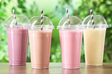 Photo of Tasty milkshakes in plastic cups on wooden table outdoors