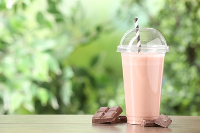 Photo of Tasty milkshake in plastic cup and chocolate on wooden table outdoors, space for text