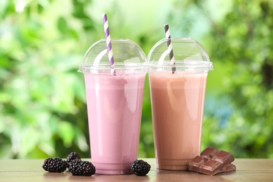 Photo of Tasty milkshakes in plastic cups and ingredients on wooden table outdoors