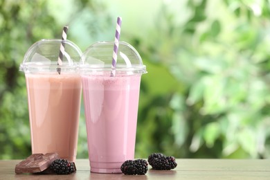 Photo of Tasty milkshakes in plastic cups and ingredients on wooden table outdoors, space for text