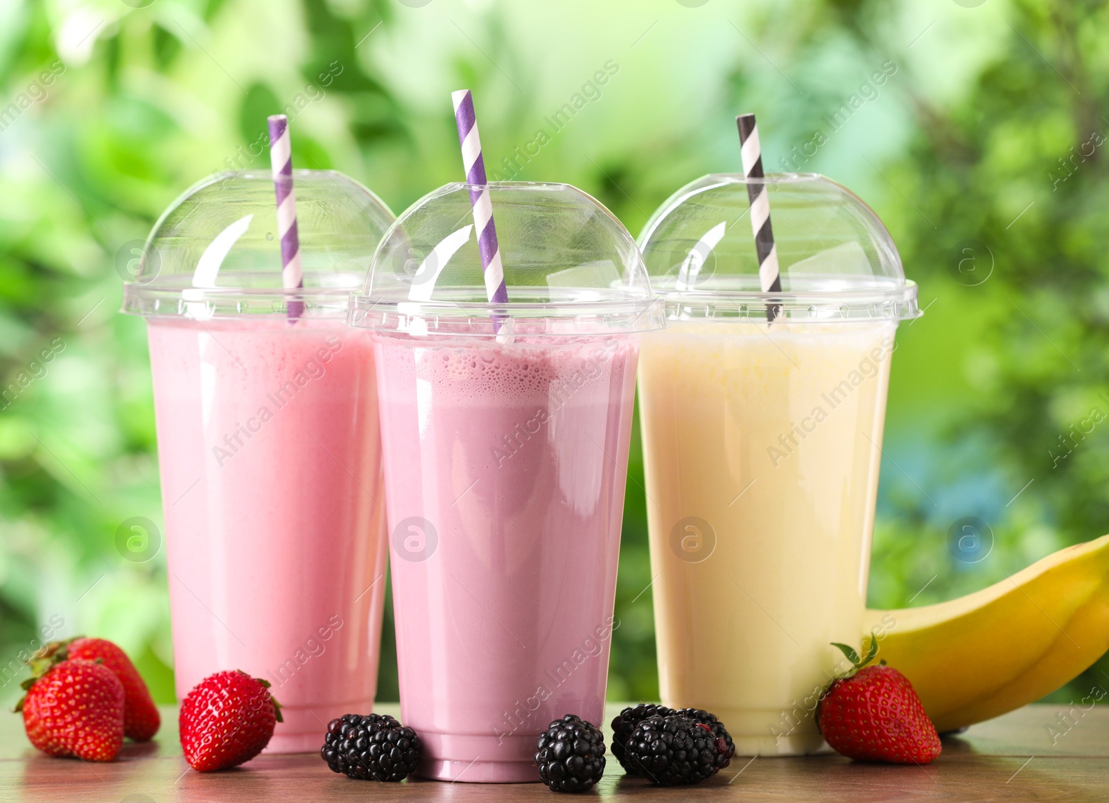 Photo of Tasty milkshakes in plastic cups and ingredients on wooden table outdoors, closeup
