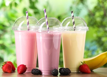 Photo of Tasty milkshakes in plastic cups and ingredients on wooden table outdoors, closeup