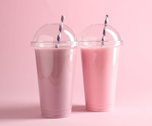 Photo of Tasty milkshakes in plastic cups on pink background
