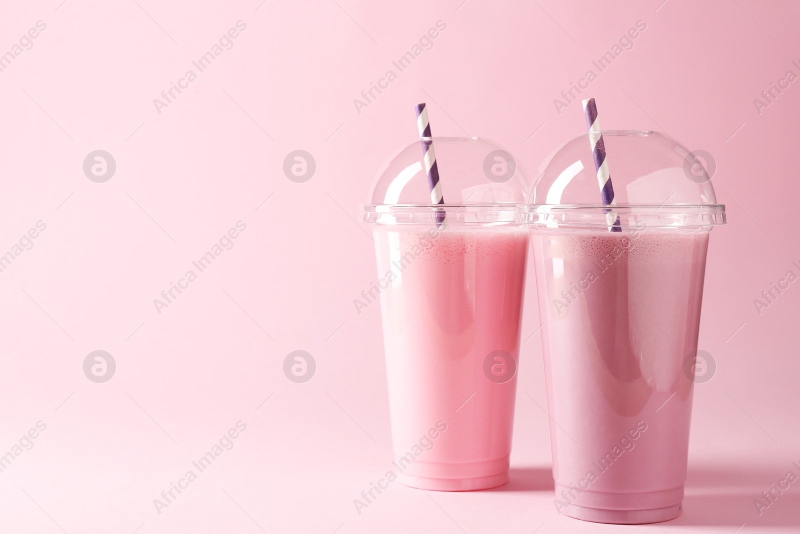 Photo of Tasty milkshakes in plastic cups on pink background, space for text