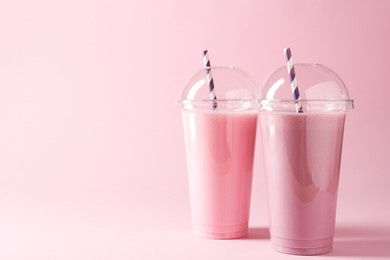 Photo of Tasty milkshakes in plastic cups on pink background, space for text