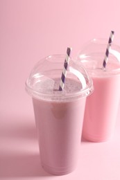 Photo of Tasty milkshakes in plastic cups on pink background
