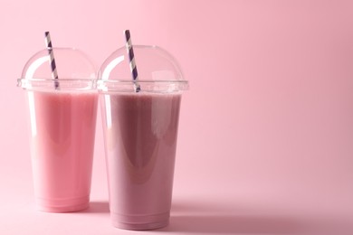 Photo of Tasty milkshakes in plastic cups on pink background, space for text