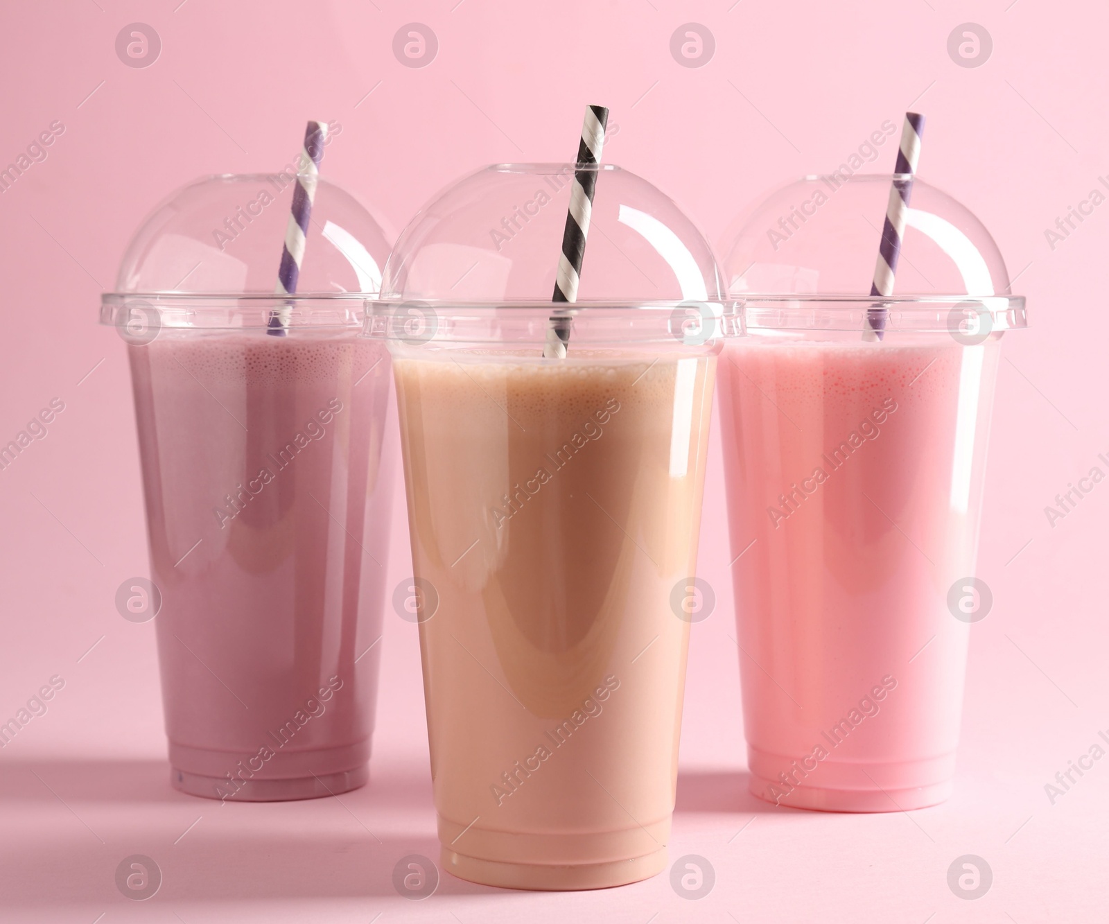 Tasty milkshakes in plastic cups on pink background Photo of Tasty milkshakes in plastic cups on pink background