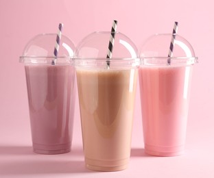 Photo of Tasty milkshakes in plastic cups on pink background