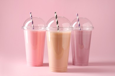Photo of Tasty milkshakes in plastic cups on pink background