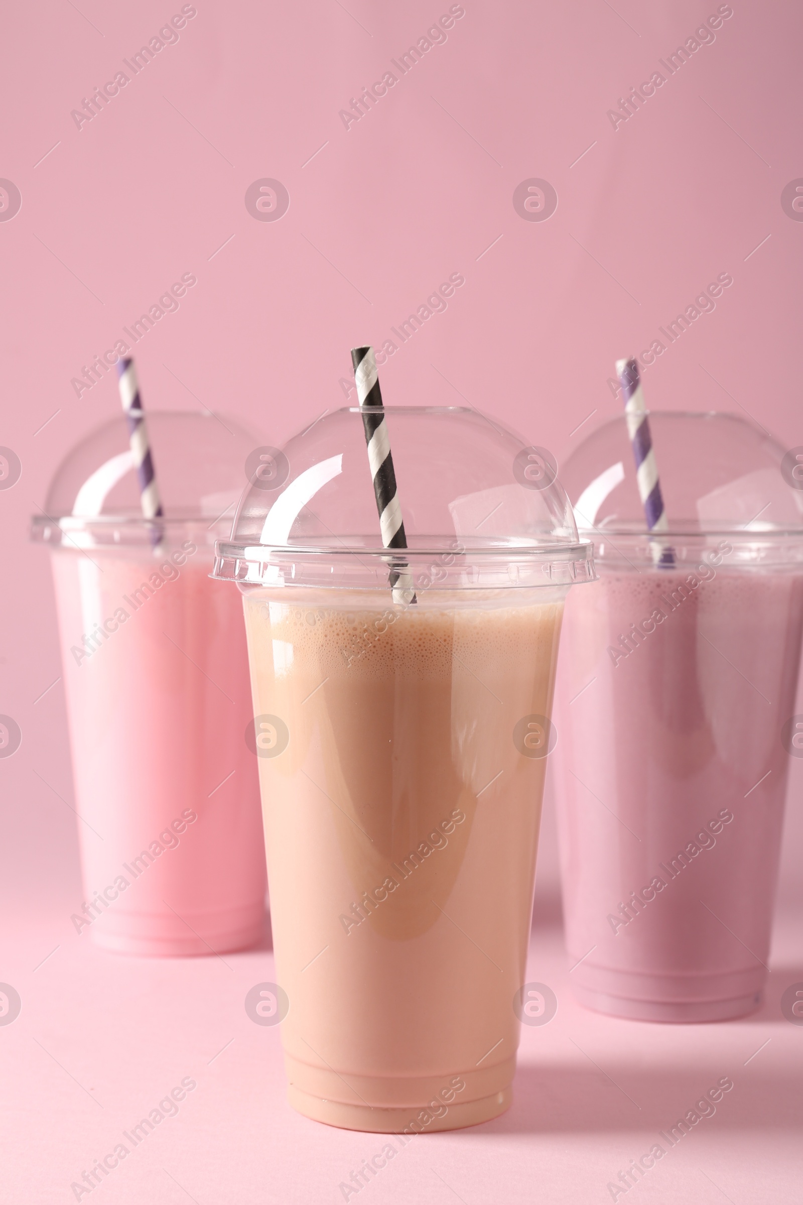 Tasty milkshakes in plastic cups on pink background Photo of Tasty milkshakes in plastic cups on pink background
