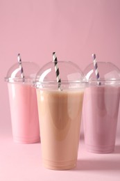 Photo of Tasty milkshakes in plastic cups on pink background