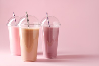 Photo of Tasty milkshakes in plastic cups on pink background, space for text