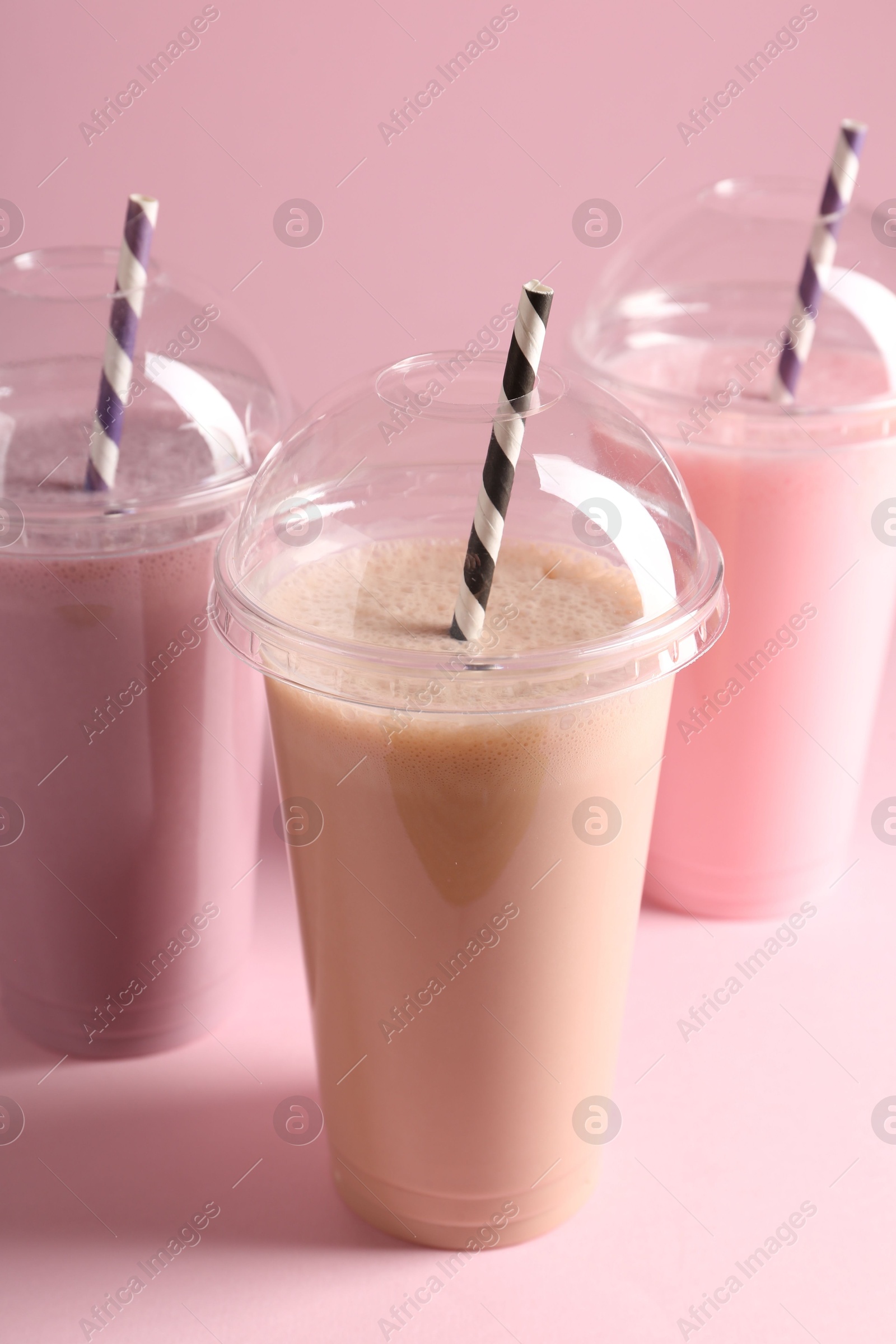 Tasty milkshakes in plastic cups on pink background Photo of Tasty milkshakes in plastic cups on pink background