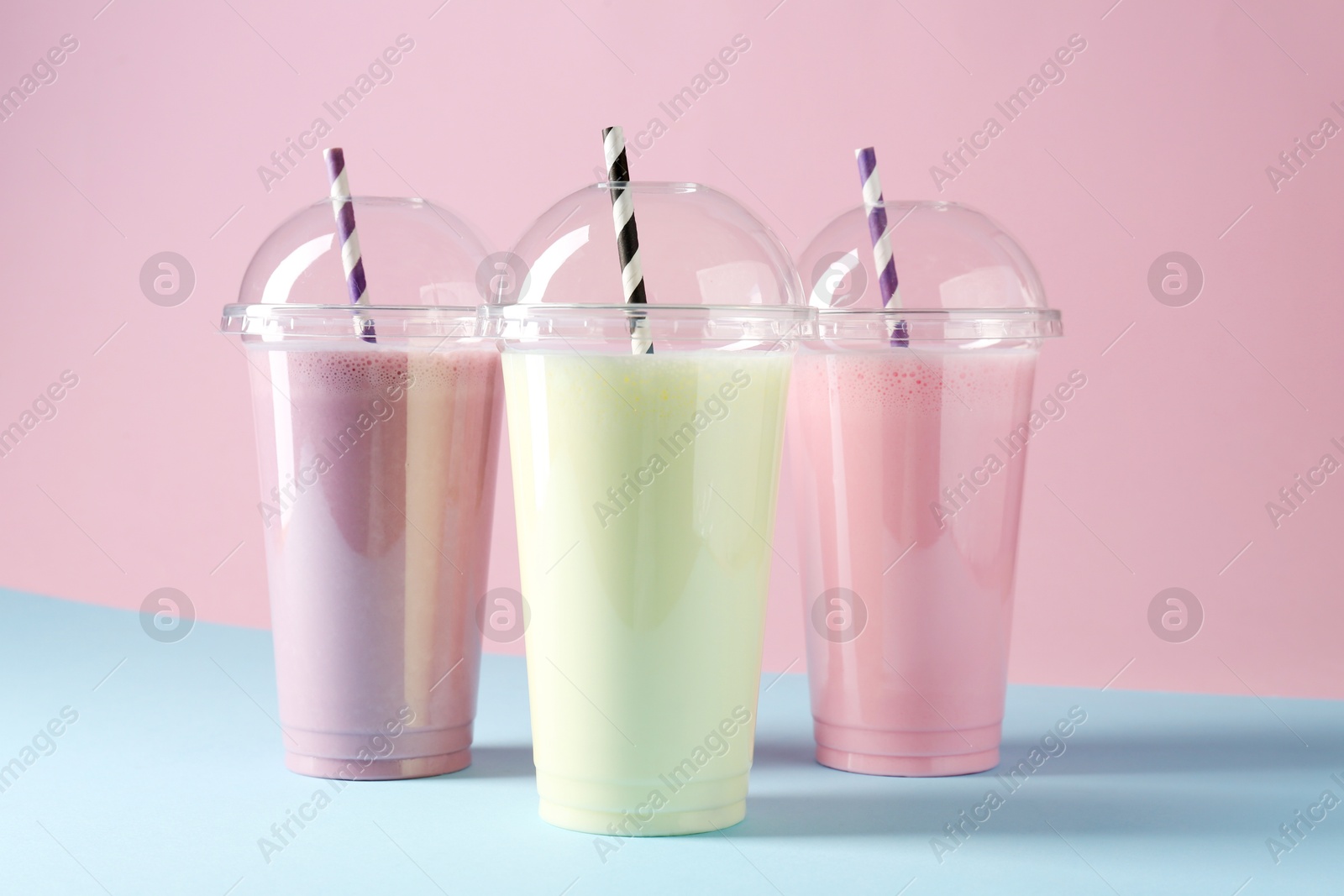 Tasty milkshakes in plastic cups on color background Photo of Tasty milkshakes in plastic cups on color background