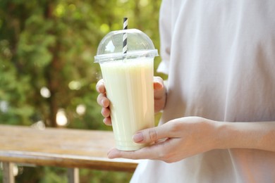 Photo of Woman holding tasty milkshake in plastic cup outdoors, closeup