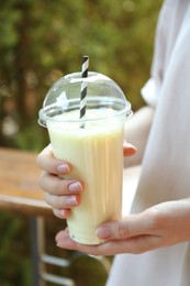 Photo of Woman holding tasty milkshake in plastic cup outdoors, closeup