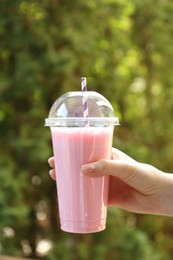 Photo of Woman holding tasty milkshake in plastic cup outdoors, closeup