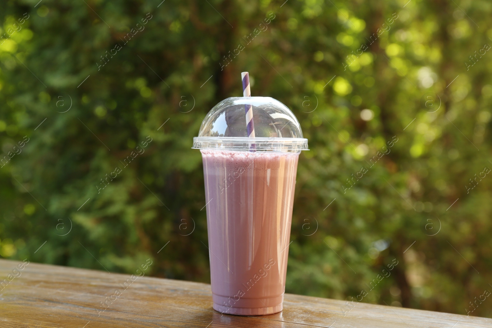 Photo of Tasty milkshake in plastic cup on wooden table outdoors