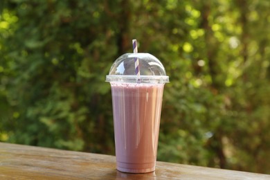 Photo of Tasty milkshake in plastic cup on wooden table outdoors