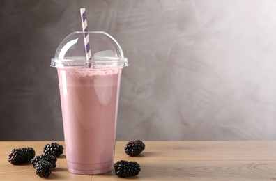 Photo of Tasty milkshake in plastic cup and blackberries on wooden table, space for text