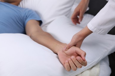 Photo of Doctor checking man's pulse with fingers at home, closeup