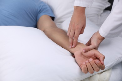 Photo of Doctor checking man's pulse with fingers at home, closeup