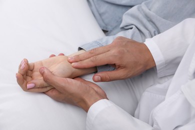 Photo of Doctor checking woman's pulse with fingers at home, closeup