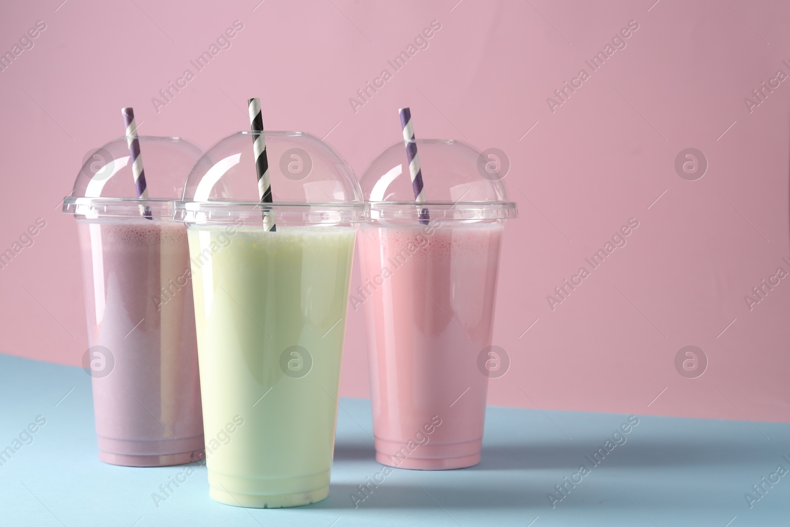 Photo of Tasty milkshakes in plastic cups on color background, space for text