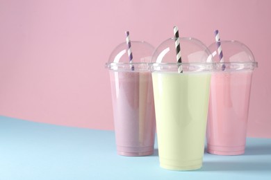 Photo of Tasty milkshakes in plastic cups on color background, space for text