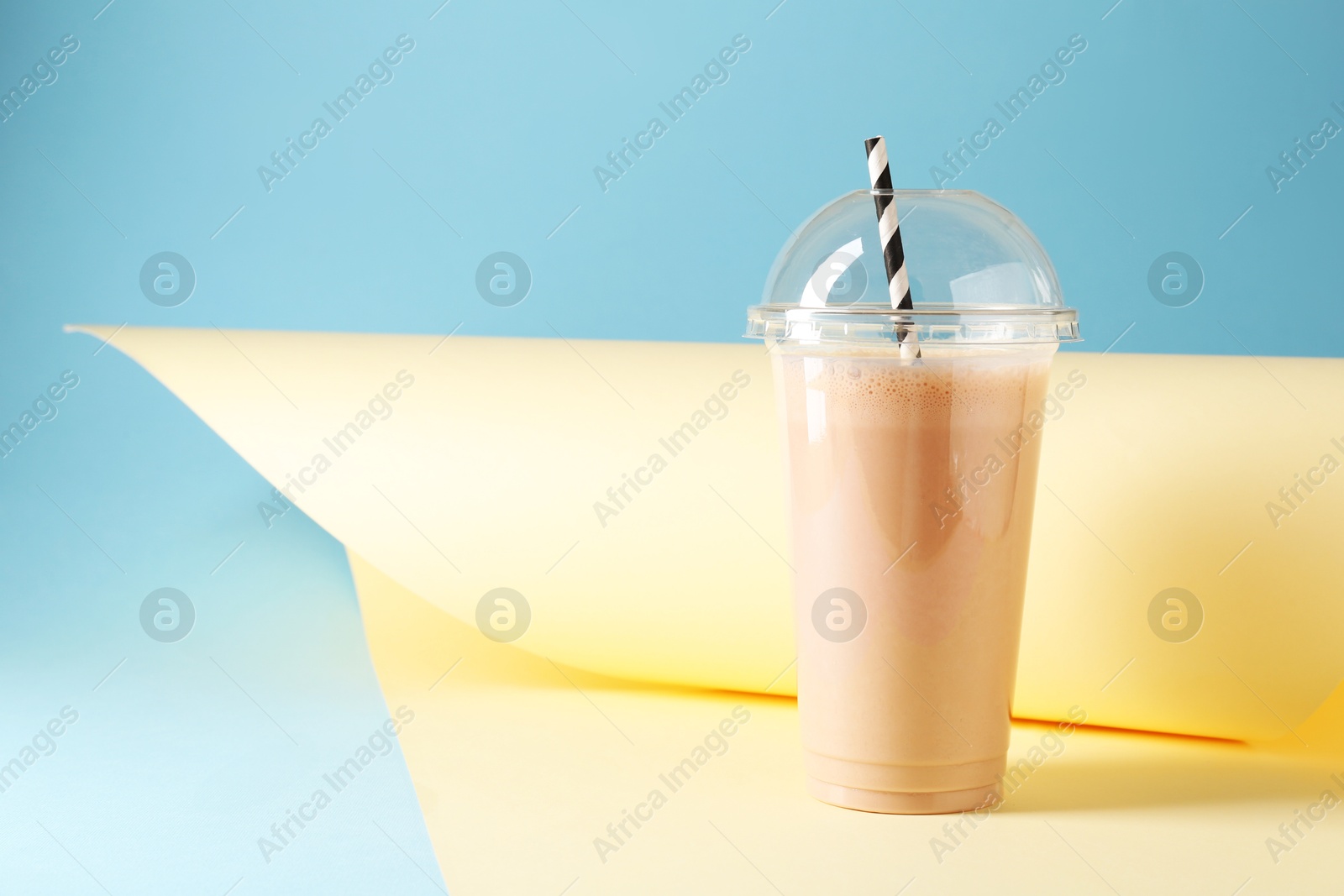 Photo of Tasty milkshake in plastic cup on color background, space for text