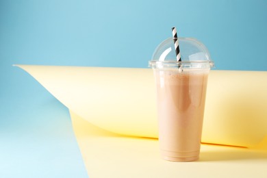 Photo of Tasty milkshake in plastic cup on color background, space for text