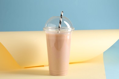 Photo of Tasty milkshake in plastic cup on color background