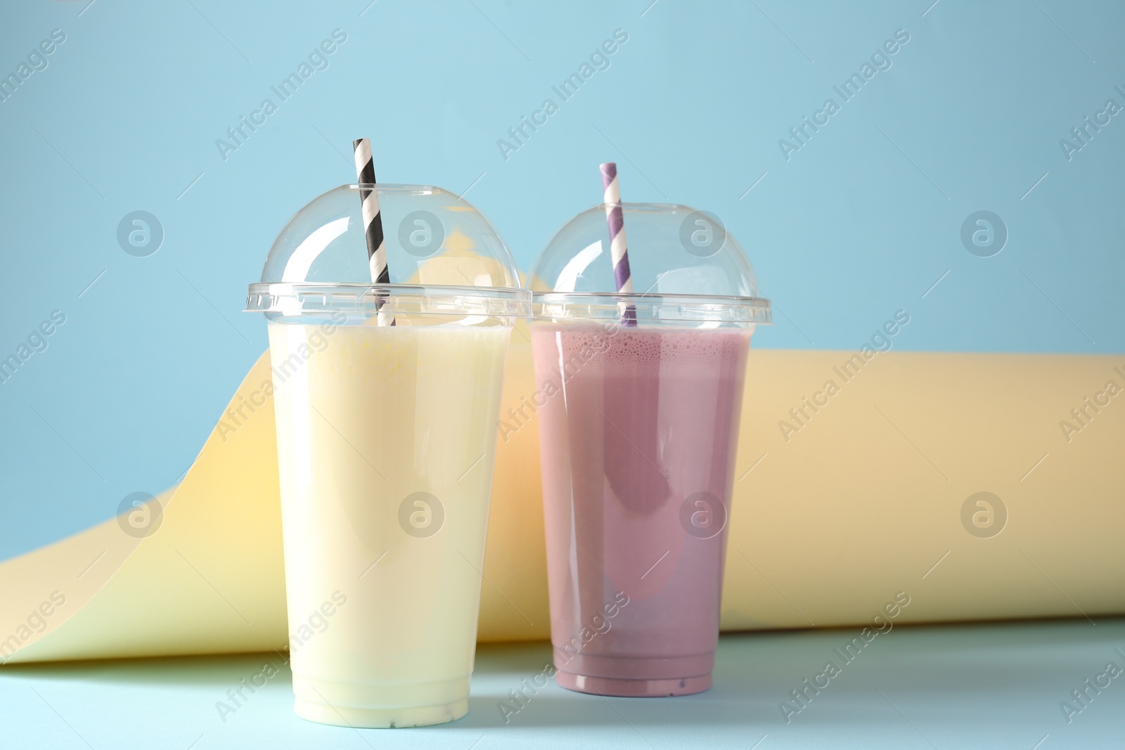 Tasty milkshakes in plastic cups on color background Photo of Tasty milkshakes in plastic cups on color background