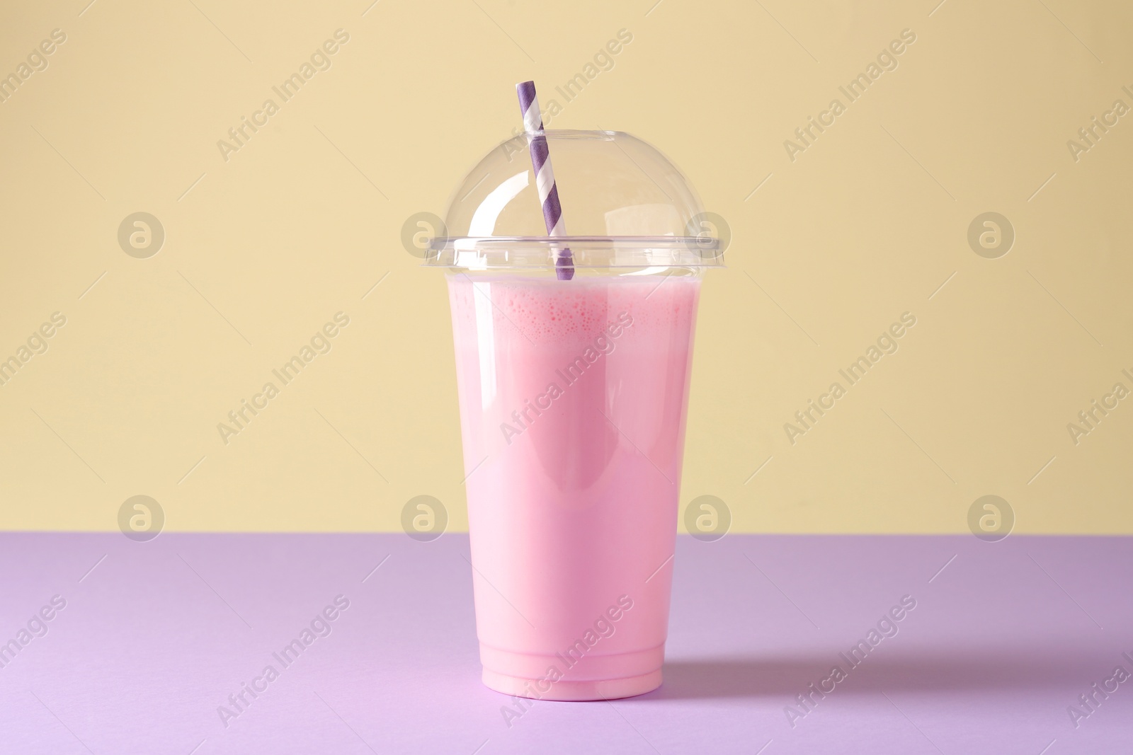 Photo of Tasty milkshake in plastic cup on color background