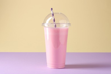 Photo of Tasty milkshake in plastic cup on color background