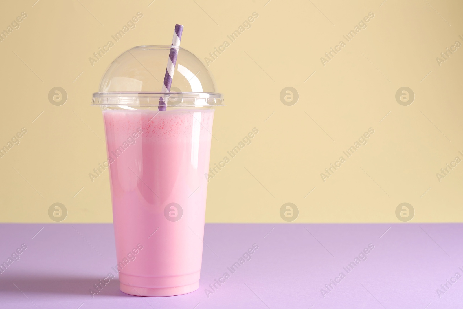Photo of Tasty milkshake in plastic cup on color background, space for text