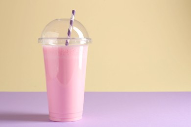 Photo of Tasty milkshake in plastic cup on color background, space for text