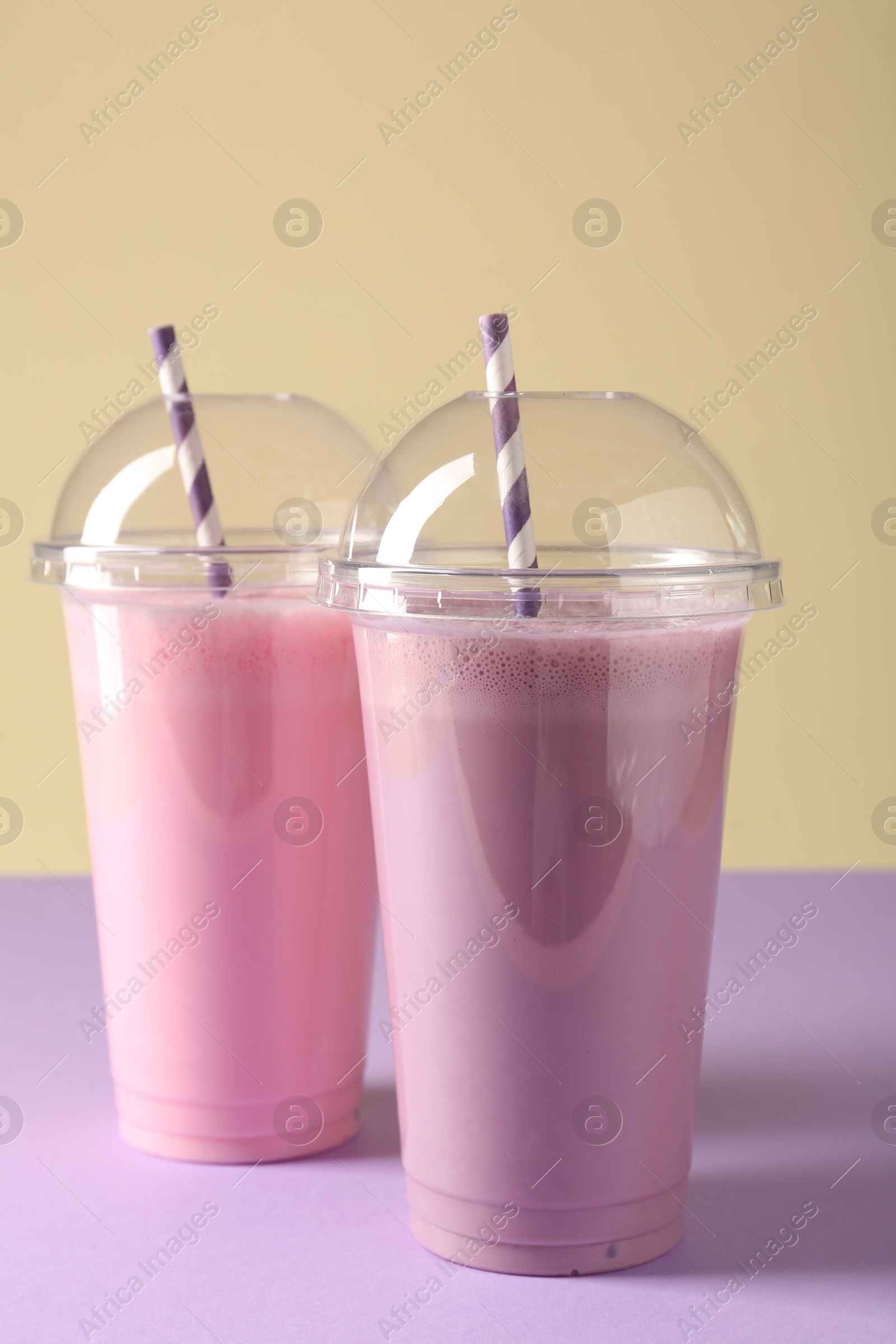 Tasty milkshakes in plastic cups on color background Photo of Tasty milkshakes in plastic cups on color background
