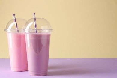 Photo of Tasty milkshakes in plastic cups on color background, space for text
