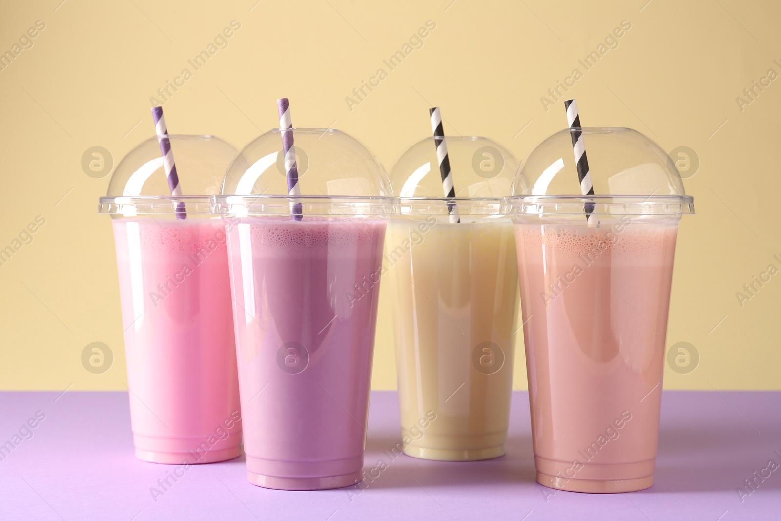 Tasty milkshakes in plastic cups on color background Photo of Tasty milkshakes in plastic cups on color background
