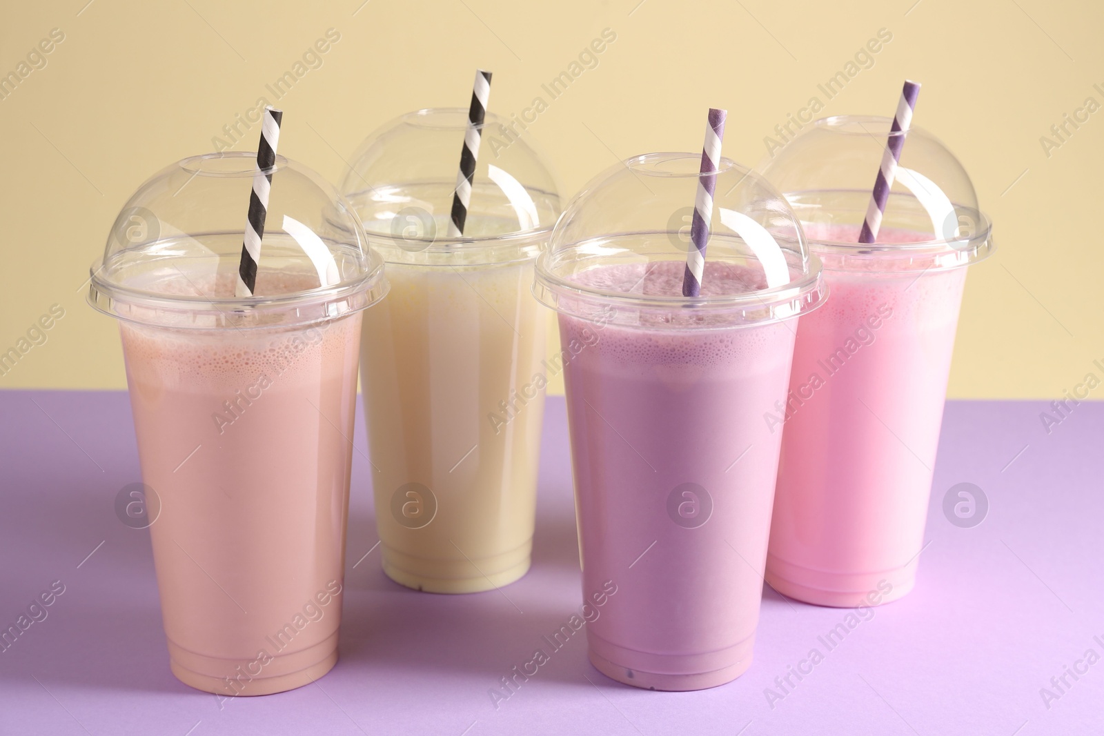 Tasty milkshakes in plastic cups on color background Photo of Tasty milkshakes in plastic cups on color background