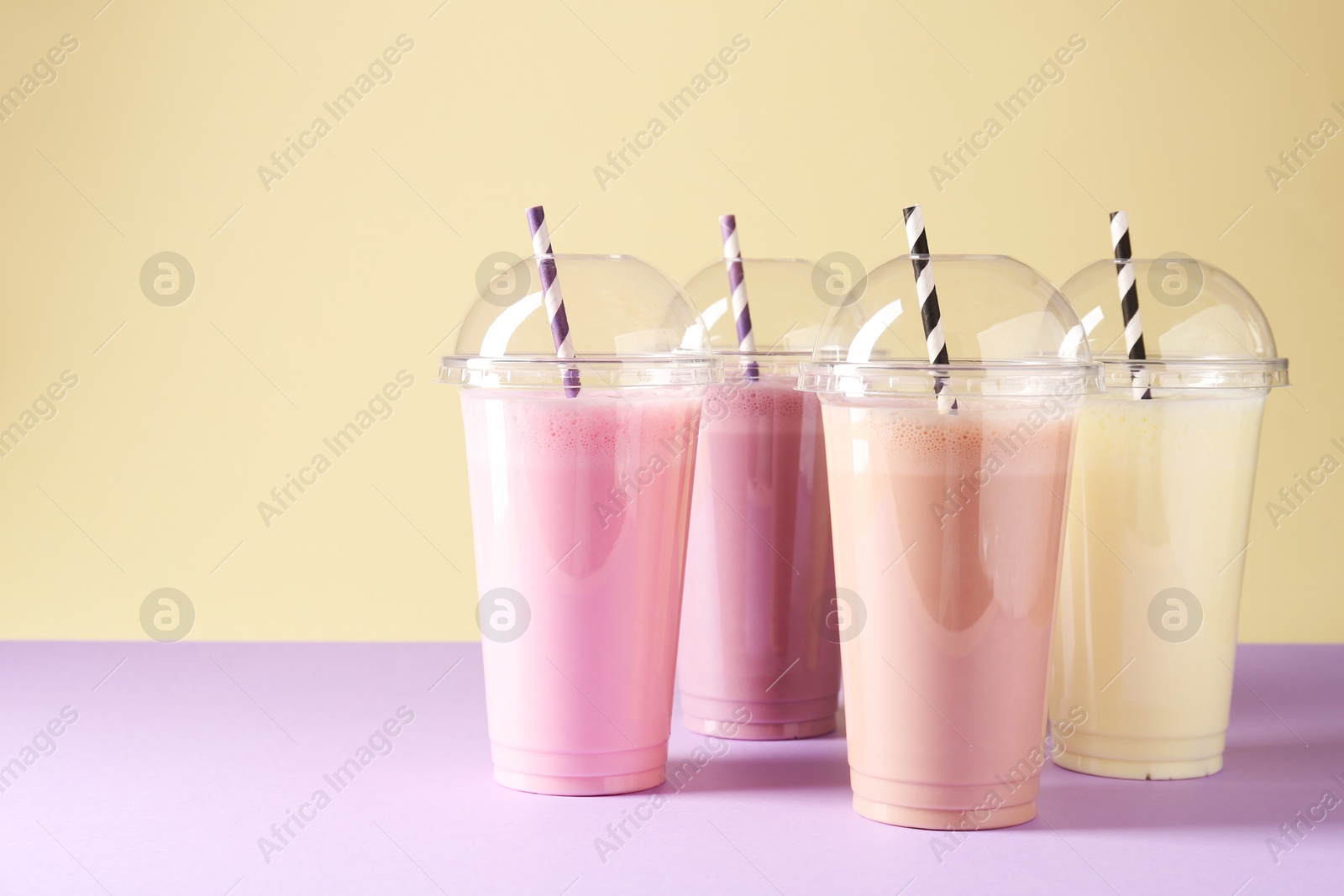 Photo of Tasty milkshakes in plastic cups on color background, space for text