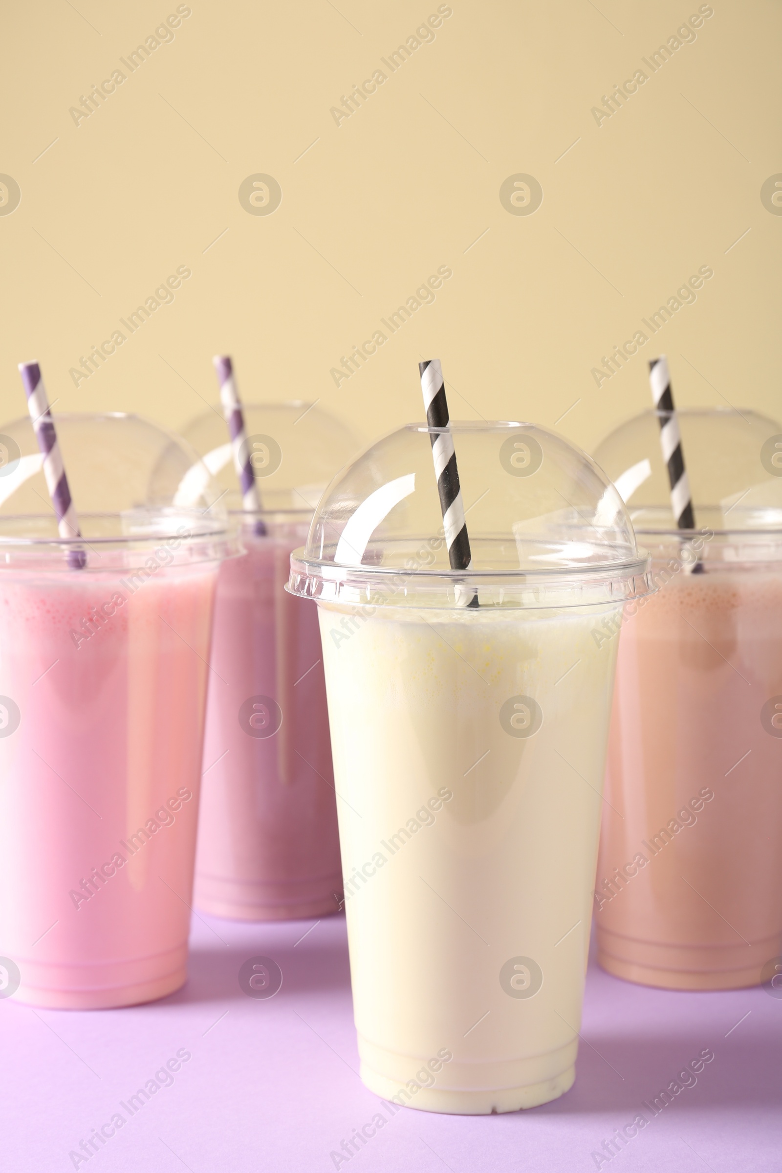 Tasty milkshakes in plastic cups on color background, closeup Photo of Tasty milkshakes in plastic cups on color background, closeup
