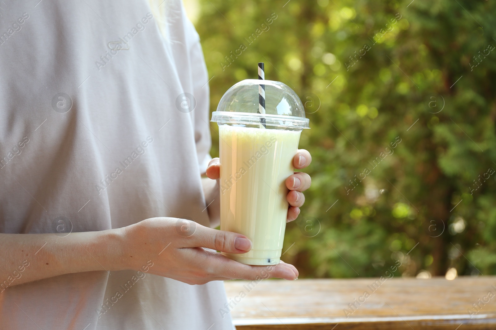 Woman holding tasty milkshake in plastic cup outdoors, closeup Photo of Woman holding tasty milkshake in plastic cup outdoors, closeup
