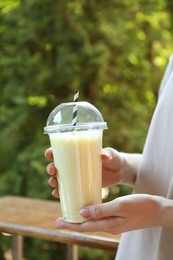 Photo of Woman holding tasty milkshake in plastic cup outdoors, closeup