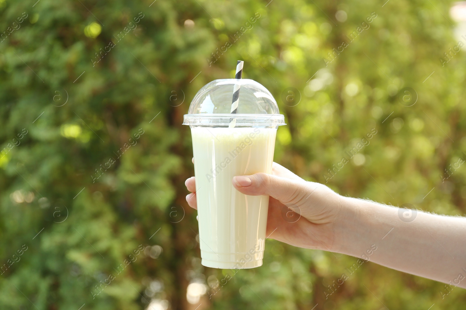 Woman holding tasty milkshake in plastic cup outdoors, closeup Photo of Woman holding tasty milkshake in plastic cup outdoors, closeup