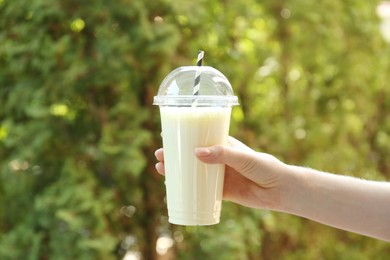 Photo of Woman holding tasty milkshake in plastic cup outdoors, closeup