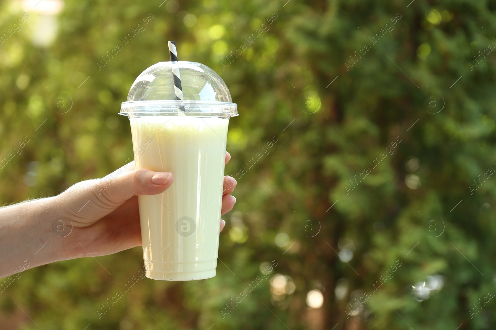 Woman holding tasty milkshake in plastic cup outdoors, closeup. Space for text Photo of Woman holding tasty milkshake in plastic cup outdoors, closeup. Space for text